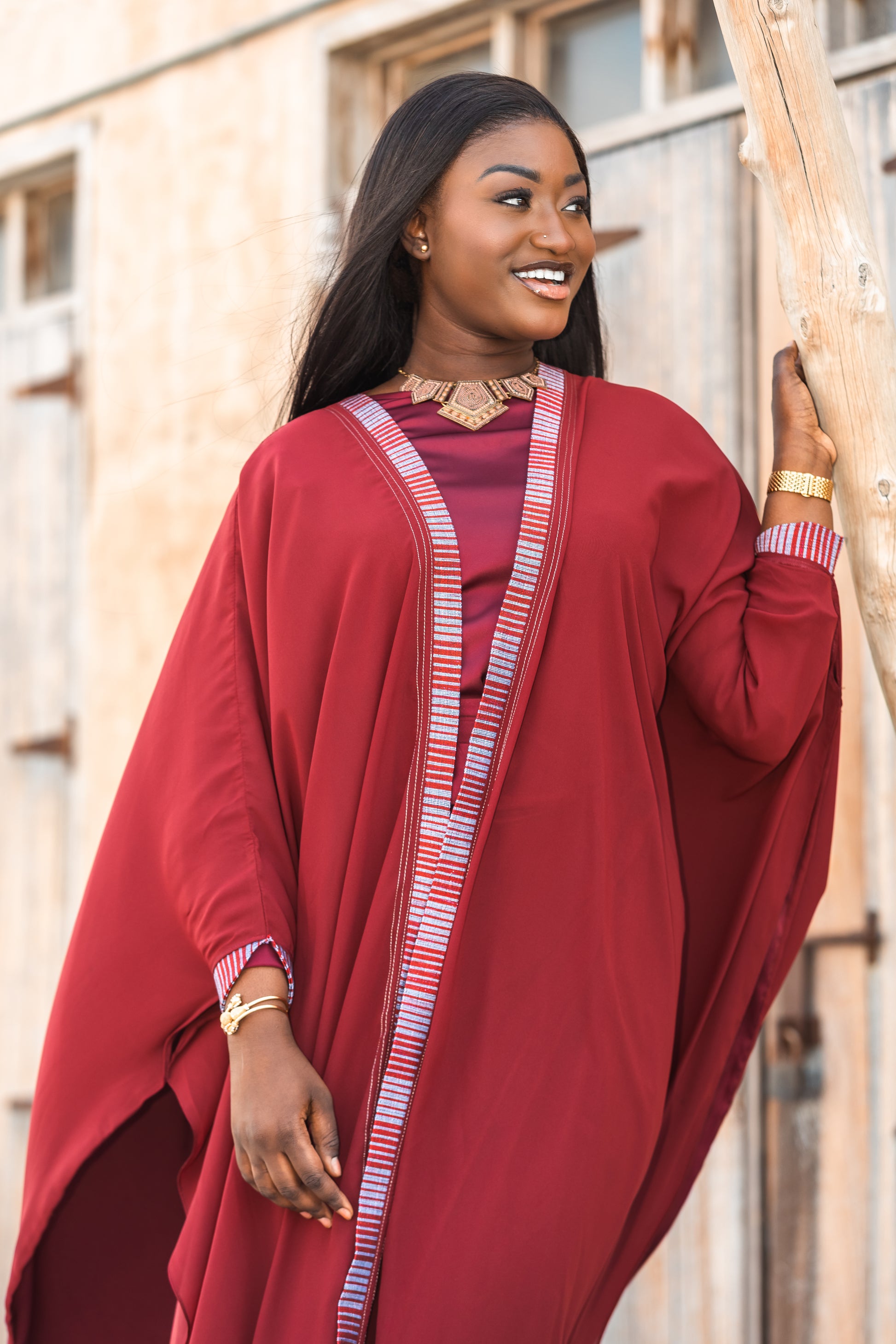 Woman wearing a red traditional outfit with a gold necklace, standing outdoors.