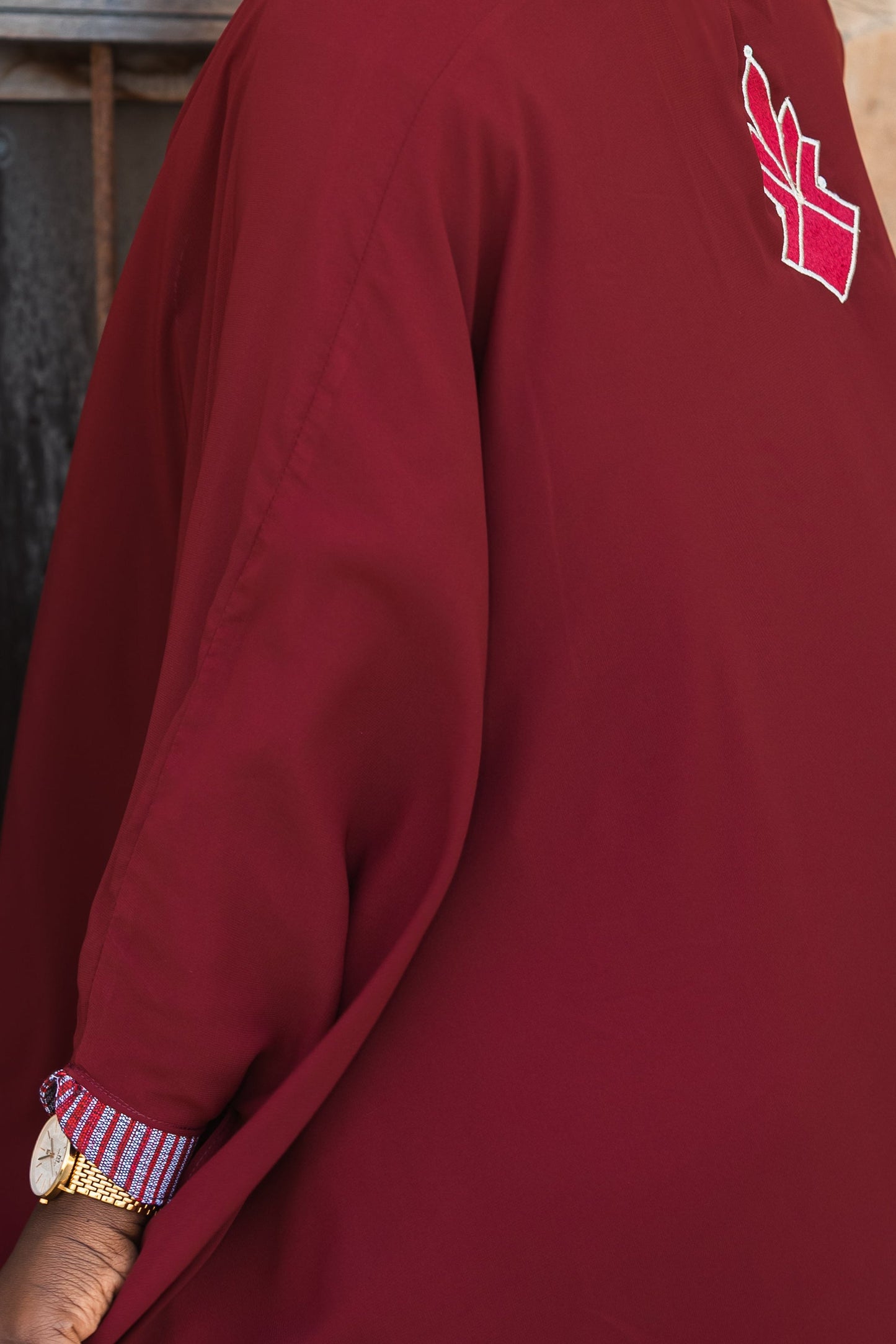 Woman in a burgundy dress with a red heart design, standing against a textured wall.