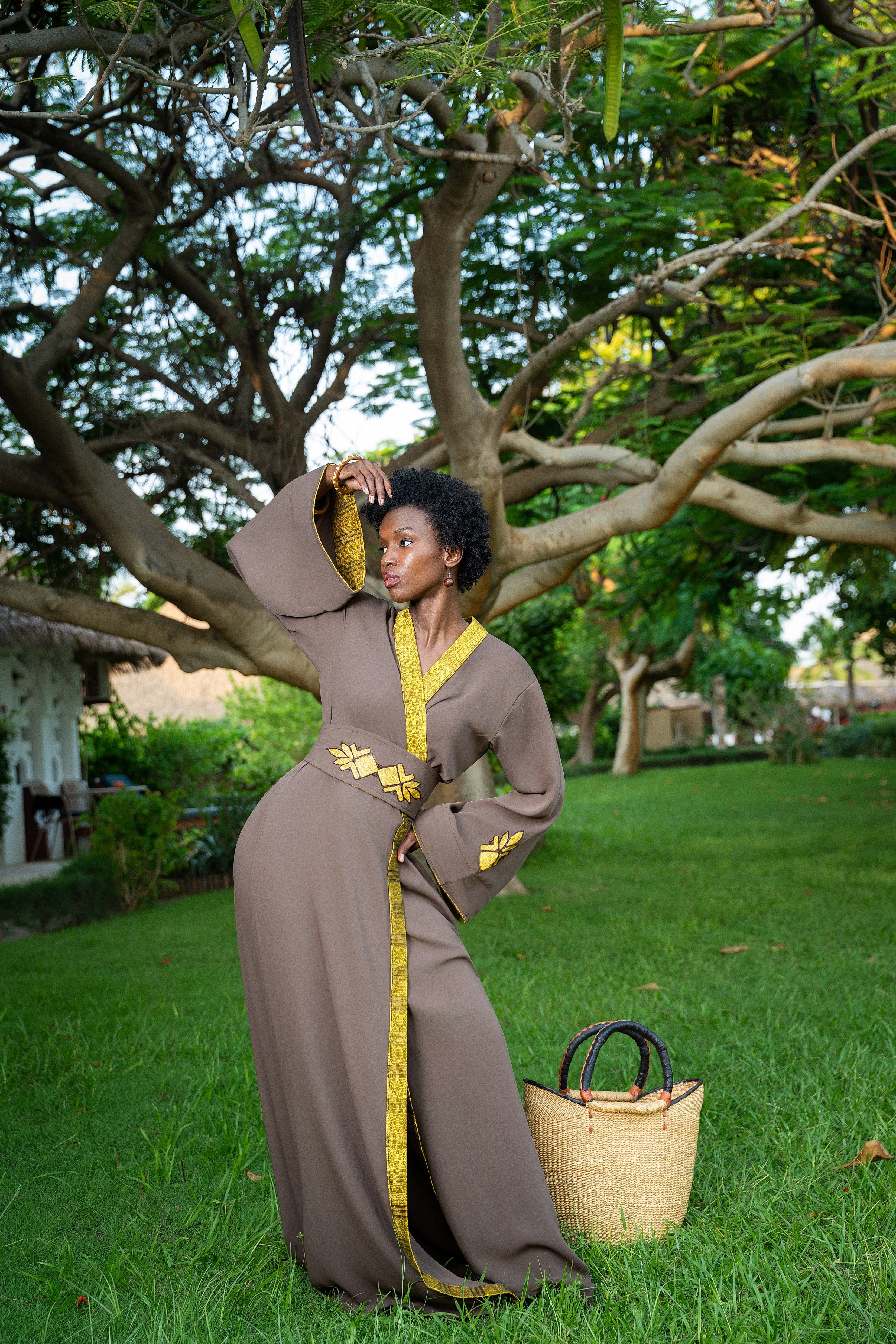 Woman in a long, brown dress with yellow accents standing in a park.